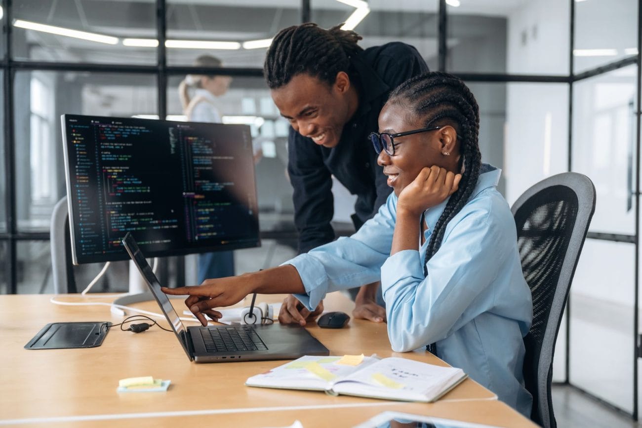 Two Black software developers reviewing code together on a laptop and monitor