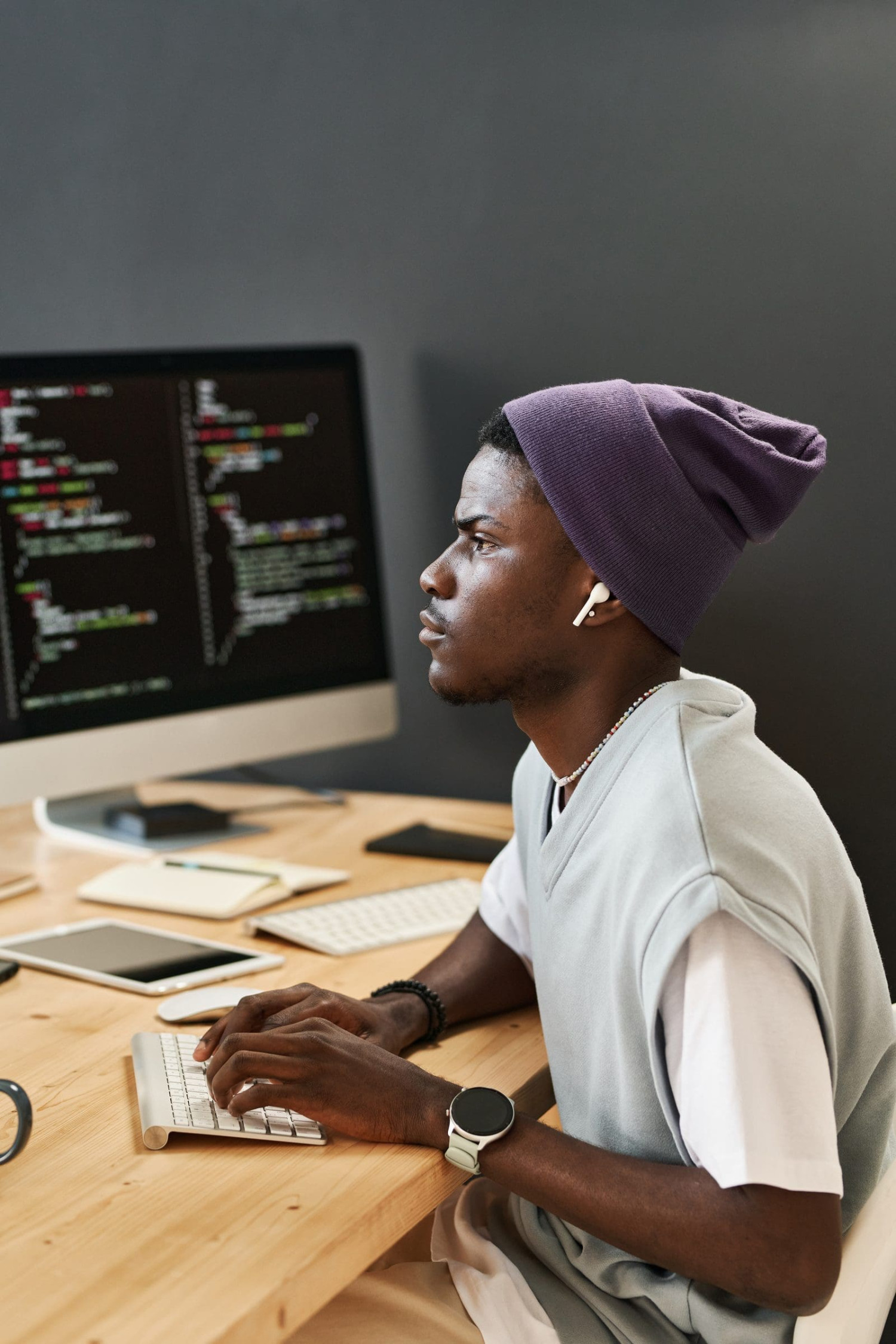 Young software developer in a beanie writing code on a desktop computer